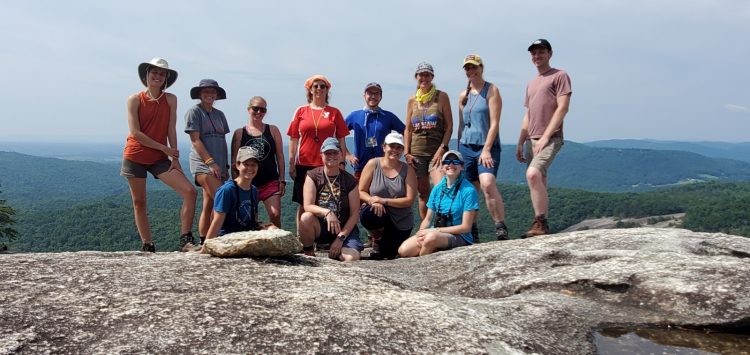 12 adults standing or sitting in two rows on top of a rock face of Stone Mountain (North Carolina) overlooking the Blue Ridge Mountains