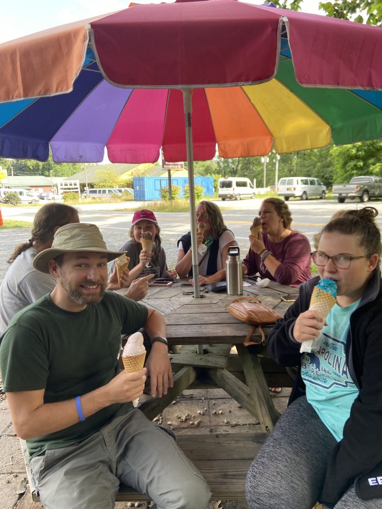 Group eating ice cream under a brightly colored umbrella.