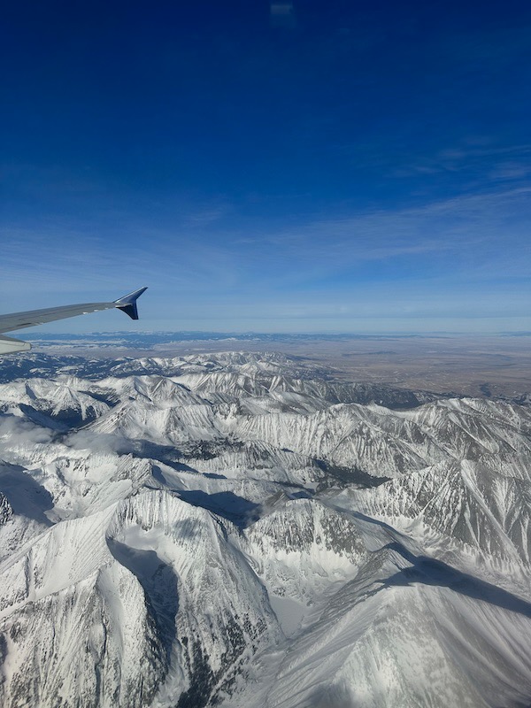 view out airplane window of snow covered mountains