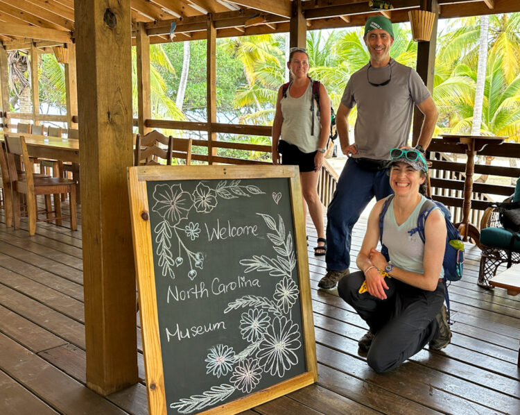 three people next to chalk board with palm trees in the background