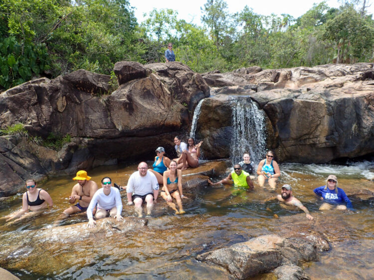 Teachers gather around the base of a small waterfall over smooth granite rocks. 
