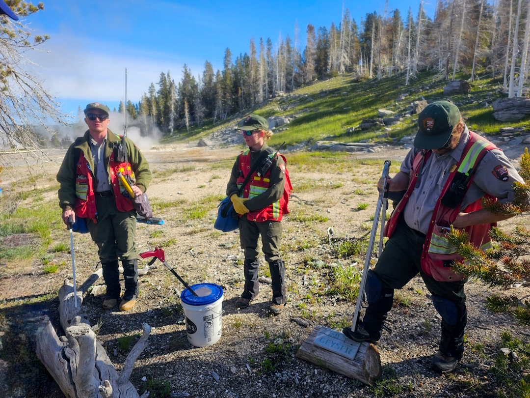 three people in NPS uniforms in front of a geyser