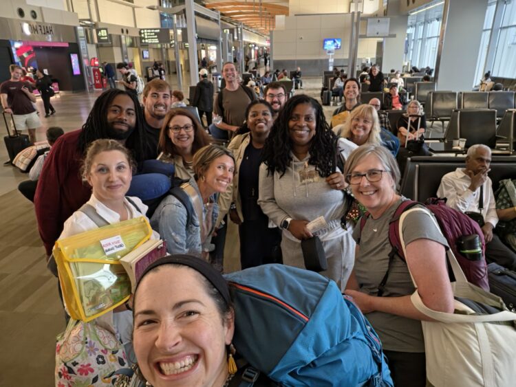 A group of educators carrying luggage stands as a group in the airport.